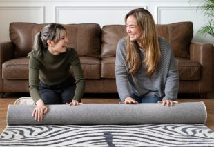 Two individuals unrolling a new area rug on a Vinyl floor in a living room.